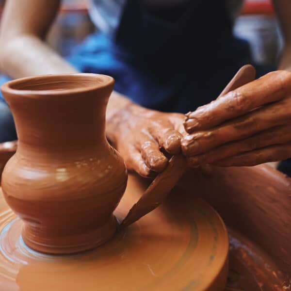 Potter using hand-tool for correcting edges of rotating jug